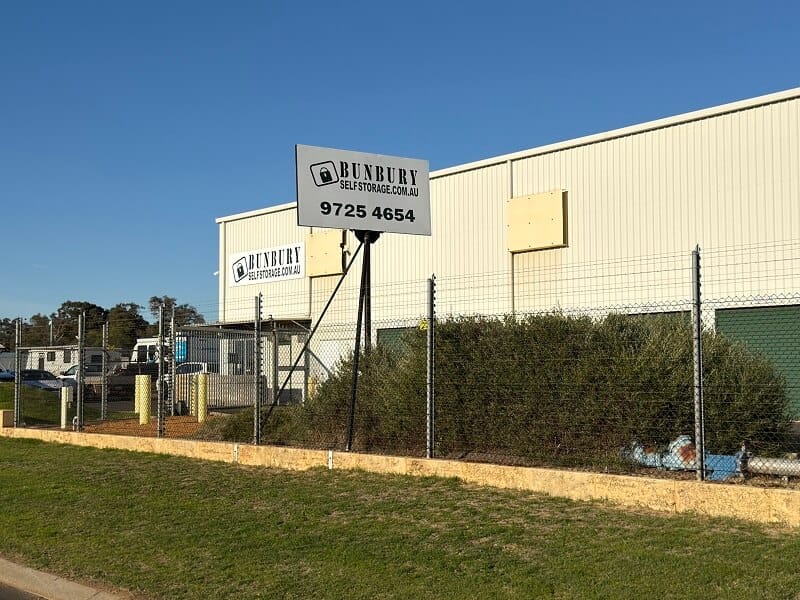 Row of green roller-door self storage units beside a paved driveway at an outdoor storage facility.