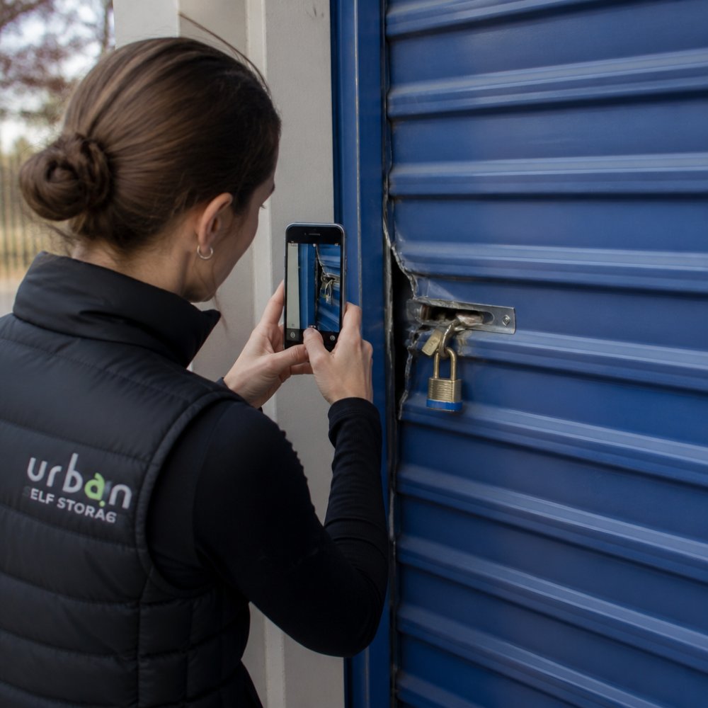 Person photographing a damaged storage unit lock for a storage insurance claim documentation process
